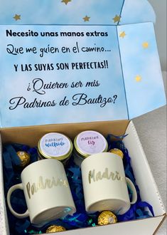 two coffee mugs in a box with confetti and chocolates on the side