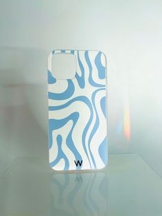 a white and blue phone case sitting on top of a glass table next to a wall