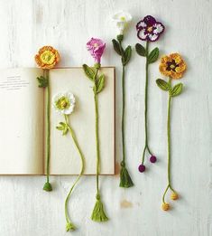 three crocheted flowers are placed next to an open book