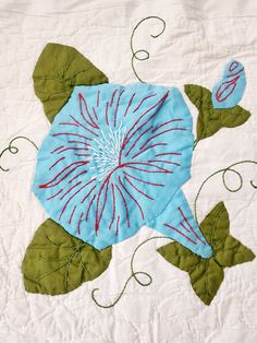 a blue flower with green leaves on a white quilt