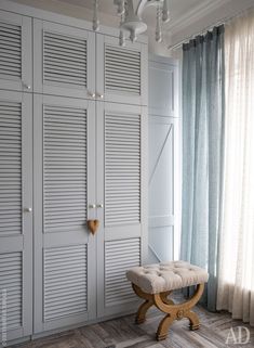 a white closet with several doors and a bench in front of it, next to a window