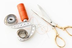 a pair of scissors, measuring tape and thread on a white surface with orange spools