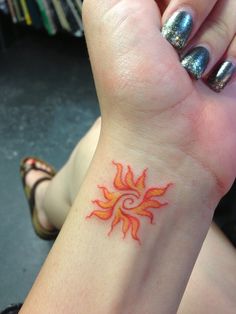 a woman's wrist with a small tattoo on her left arm and the sun in the middle