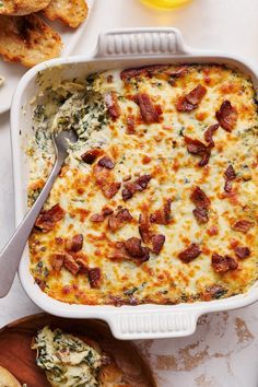 a casserole dish with spinach and bacon in it on a table next to bread