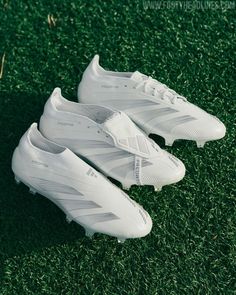 two white soccer shoes sitting on top of green grass