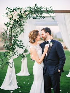 a bride and groom standing under an arch decorated with white flowers at their wedding ceremony