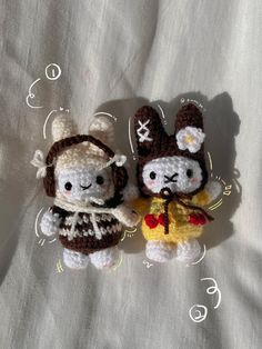 two small crocheted stuffed animals sitting next to each other on a white sheet