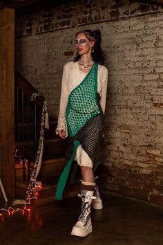 a woman in white shirt and green scarf standing on stairs with lights behind her,