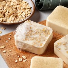 four bars of soap sitting on top of a wooden cutting board next to a bowl of oats