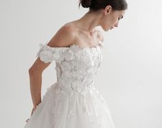 a woman in a white wedding dress with flowers on the skirt and off - shoulder