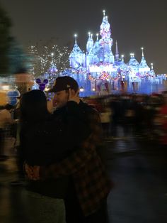 a man and woman standing next to each other in front of a castle at night