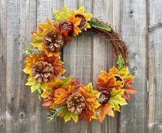 a wreath made out of leaves and acorns on a wooden fence with pine cones