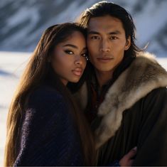 a man and woman standing next to each other in front of snow covered mountains with their arms around each other