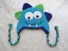 a crocheted blue hat with an evil face and green horns on the side