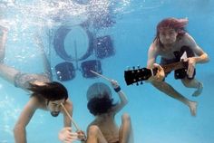 two people playing guitars in the water while another person swims behind them and watches