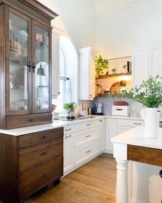 a kitchen with white cabinets and wood floors is pictured in this image, there are plants on the counter