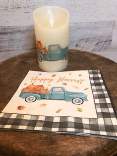 a candle sitting on top of a wooden table next to a napkin with an image of a truck