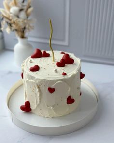 a white cake with red hearts on it sitting on a plate next to a vase