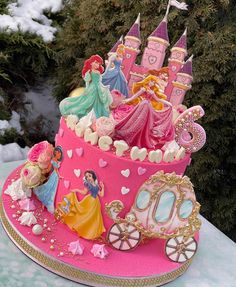 there is a pink cake decorated with princesses and carriages on the table in front of snow covered trees