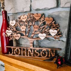 a wooden family tree with names and hearts on it next to a red vase, framed by a brick wall