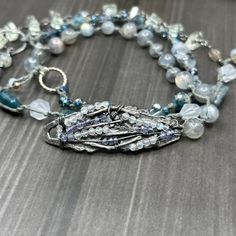 This incredible wrap bracelet has been a work in progress for a while. The combination of the pewter focal with the gorgeous 6mm flashy labradorite rounds absolutely enchanted me. From there, I added so many of my favorite things. In this bracelet, you’ll find apatite rectangles, the most insane faceted 8mm kyanite, 8mm starcut pale jade, flashy tourmilinated rainbow moonstone, smoky quartz, and the most incredible faceted prasiolite nuggets. Also featured are the prettiest faceted glass rondelles. Let’s circle back to the focal. The shape was so interesting and mysterious to me. I wrapped on faceted labradorite and iolite to bring out some of the lines. This wrap bracelet is sterling silver, with the exception of the USA made pewter focal. The knotted portion of the bracelet was done in h Bar Bracelets, Hook Clasp, Faceted Glass, Smoky Quartz, Rainbow Moonstone, Work In Progress, My Favorite Things, Wrap Bracelet, Moonstone