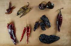 several different types of chili peppers on a wooden surface with black pepper pods and other vegetables