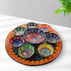 a plate with many different colored bowls on it next to a potted plant in the background