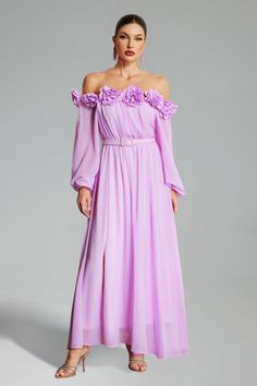 a woman in a long purple dress with flowers on the shoulders and shoulder, standing against a