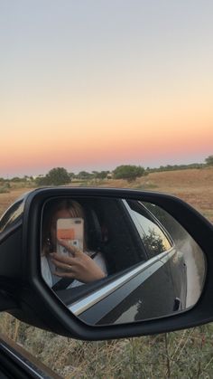 a woman taking a selfie in the side view mirror of a car with her cell phone