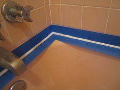 a bathroom sink with blue tape on the edge and brown tile around it, under a faucet