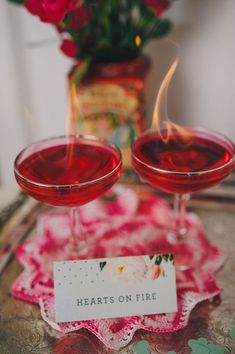 two glasses of wine sitting on top of a table next to a vase with flowers