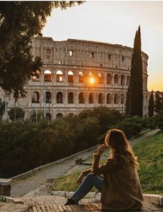 a woman sitting in front of the colossion at sunset with her hands on her head