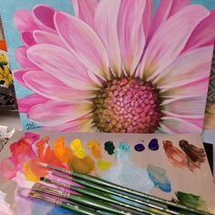 a pink flower sitting on top of a table next to paints