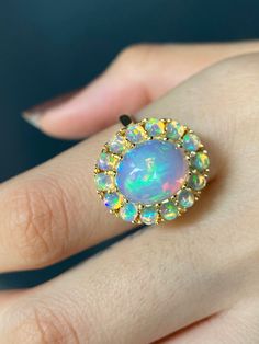 RING DETAILS: ✪Design: Gold ring ✪Gemstone: Opal ✪Gemstone shape: Cabochon oval ✪Gemstone size: Center stone: 12x10mm Oval, side stones: 3mm round ✪Setting type: Cluster ✪Metal type: 14k solid yellow gold (also available in white and rose gold, please select at checkout) ✪Total ring weight: 7 grams ✪Metal finish: Smooth shiny Choose your ring size from drop down menu and if you need any other preferred ring size please contact us. QUALITY OF MATERIALS: Metal: Most of our jewelry at JewelryMansio Yellow Gold Cluster Rings With Multi-stone, Fine Jewelry Multi-stone Round Cut Opal Ring, Fine Jewelry Opal Ring With Multi-stone Round Cut, Multi-stone Opal Promise Ring, Fine Jewelry Multi-stone Round Halo Ring, Fine Jewelry Multi-stone Halo Ring, Multi-stone Round Halo Ring Fine Jewelry, Opal Multi-stone Round Cut Rings, Oval Multi-stone Cluster Ring Fine Jewelry