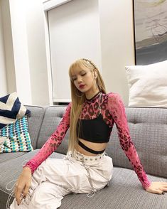 a woman sitting on top of a couch wearing white pants and a pink shirt with leopard print