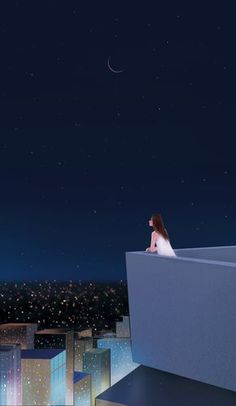 a woman sitting on top of a building looking at the night sky over a city