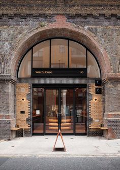 a person standing in front of a brick building with an arched doorway and glass windows