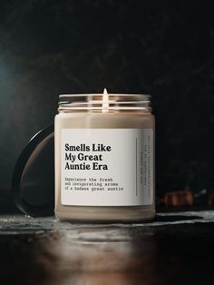 a candle sitting on top of a wooden table next to a black mug with the words smells like my great aumite era