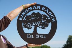 a man holding up a sign that says kingman ranch est 2004 with a tree on it