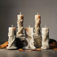 four candles are sitting on the ground with leaves around them