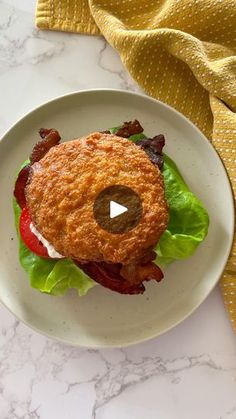 a burger with bacon and lettuce on a white plate next to a yellow napkin