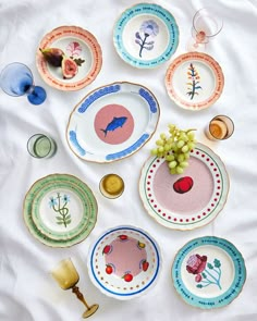 there are many plates on the table with flowers and fruit painted on them in different colors