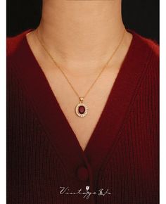 a woman wearing a red sweater with a gold necklace on her neck and an oval shaped pendant