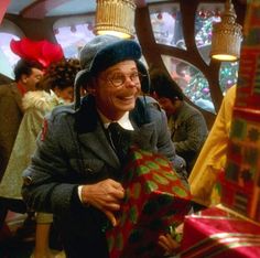 an older man holding a christmas present in front of a large group of people at a party