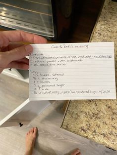 someone holding up a piece of paper with writing on it in front of an oven