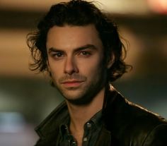 a man with long curly hair wearing a black leather jacket and looking at the camera