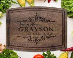 personalized cutting board engraved with name and date surrounded by fresh vegetables on white background