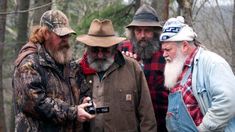 three men with long beards and hats are standing in the woods looking at a camera