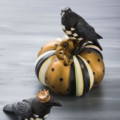 two black birds sitting on top of a pumpkin shaped object next to another bird figurine