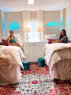 two women sitting on twin beds in a room with rugs and lights above them